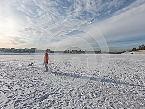 woman with winter coat walk the dog on frozen lake with thick snow in winter