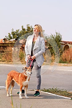 Woman in walk with his Shetland sheepdog dog on leash. Dog walker standing, posing in front of camera.
