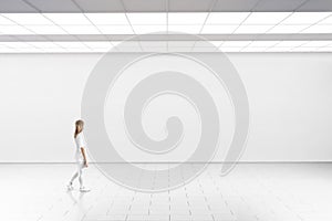 Woman walk in museum gallery with blank wall. photo