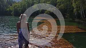 Woman walk on water on pier in sunglasses and a boho silk shawl. Girl rest on flood wood underwater dock. The pavement