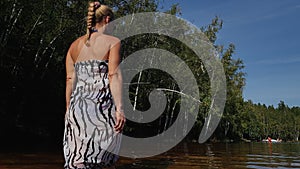 Woman walk on water on pier in sunglasses and a boho silk shawl. Girl rest on flood wood underwater dock. The pavement