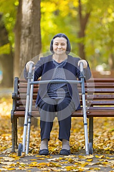 Woman with walker on bench smiling at camera outdoors