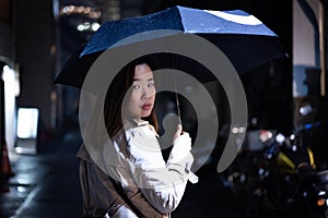 A woman is walking alone at the night street in the rainy season