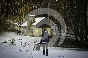 Woman walking alone towards a wooden cabin in the middle of a snowy forest