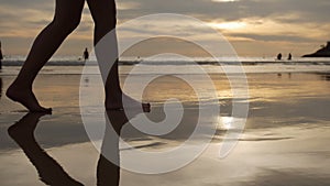 Woman walking along beach barefoot over sunset