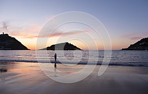 Woman walking along the beach and bay of La Concha, sunset in the city of Donostia-San Sebastian, Basque Country