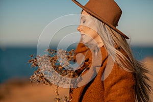 A woman walking along the coast near the sea. An elegant lady in a brown coat and a hat with fashionable makeup walks on