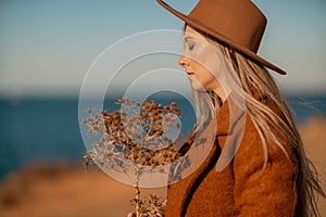 A woman walking along the coast near the sea. An elegant lady in a brown coat and a hat with fashionable makeup walks on