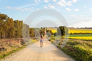 Woman walking along a dusty road among the rural fields