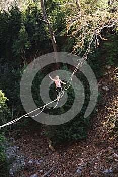 A woman is walking along a stretched sling over a forest