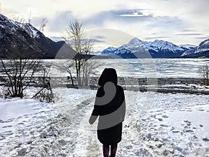 A woman walking along an unknown path towards a frozen lake in a beautiful winter landscape on Abraham Lake, Alberta, Canada.