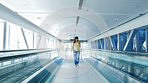 Woman walking between automatic walkways, in subway crossing, using her phone, a mean of communication, a fashionable
