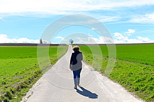 Woman walking away along a road through fields