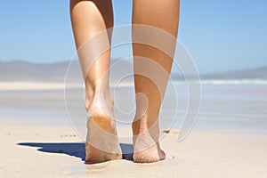 Woman walking barefoot on beach from behind