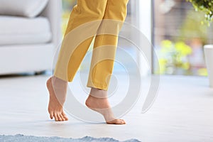 Woman walking barefoot at home, space for text