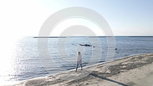 Woman walking on the beach by the sea on a sunny winter day, orbit shot with drone