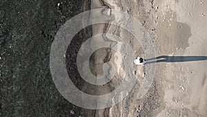 Woman walking on the beach by the sea on a sunny winter day, tracking drone shot