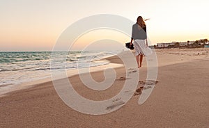 Mujer caminando lejos de la arena de la playa de la puesta de sol de mar el agua de mar de las vacaciones de verano.