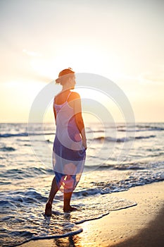 Woman walking on the beach in the surf at sunset