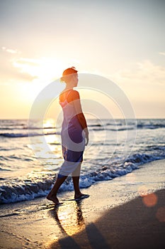 Woman walking on the beach in the surf at sunset