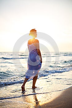 Woman walking on the beach in the surf at sunset
