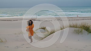 Woman walking beach twilight with orange flowers. Girl with bouquet on seashore.