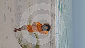 Woman walking beach twilight with orange flowers vertical. Girl with bouquet