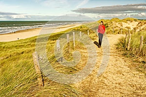 A woman walking on a beautiful sandy trail along the ocean. North Holland dune reserve, Egmond aan Zee, Netherlands