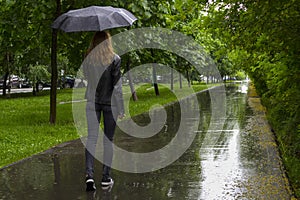 Woman walking with black umbrella under the rain in a park