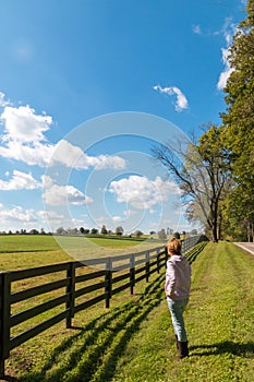 Woman walking country road along horse farms