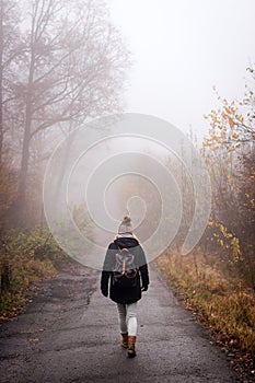 Woman walking on country road in fog at autumn morning