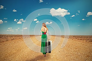 Woman walking through desert talking on phone carrying suitcase