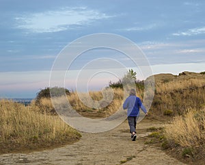 Woman walking on dirt path amid sandstone rocks and dried grass