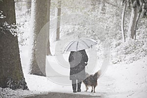 Woman walking dog in snowing forest