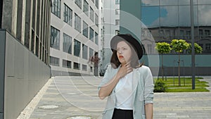 A woman walking down the street and coughing. A woman with signs of illness coughs and covers her mouth with her hand