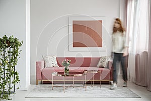 Woman walking in a feminine living room interior with a sofa, coffee table and painting