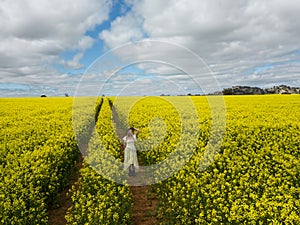 Woman walking through a field of yellow canola flowers