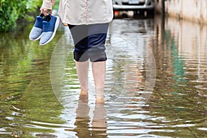 Woman walking on flooding road with holding shoes after the heavy rains,cause of itchy skin include,be careful of leptospirosis,it