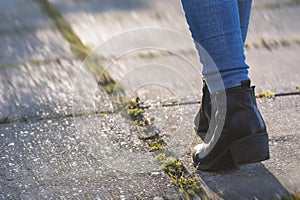 Woman walking forward in the park, moving feet in leather boots at sunset. Leisure activity, walking concept