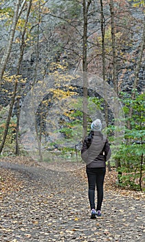 woman walking on a hiking trail in Taughannock Falls State Park wearing brown jacket, hat