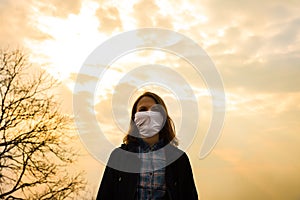 Woman is walking in mask in the nature. Coronavirus protection. No people around. Girl is keeping the distance. Beautiful sky on