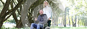 Woman walking in park with disabled man in wheelchair