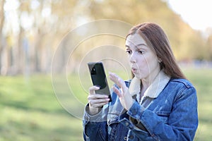 Woman walking through the park looking at her smartphone in surprise