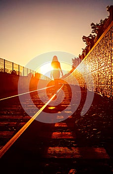 Woman is walking on a railways in the rays of a sunset