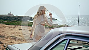 Woman walking retro car at sunny sea coast. Girl traveler relaxing on seashore.