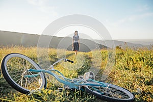 Woman walking on rural road to bicycle in the foreground outdoor.