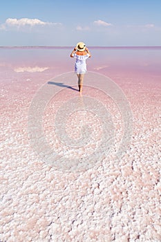 Woman walking on salt plains. Water colored with pink algae