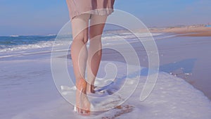 Woman walking on sand beach, ocean waves on background, back view