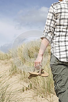 Woman walking in sand dunes holding sandals