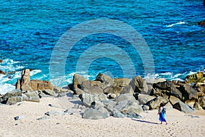 Woman walking on sandy beach by rocky Sea of Cortez coastline.